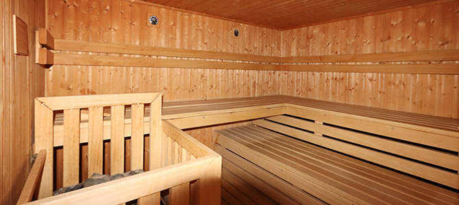 Holzgetäfelter Innenraum der Sauna mit Sitzbänken und einem Steinofen in der Ecke.
